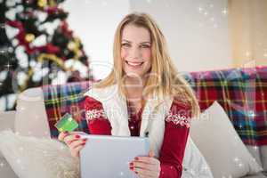 Composite image of cute blonde sitting on couch holding credit c