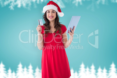 Composite image of festive brunette holding credit card and tabl