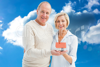 Composite image of happy mature couple with model house