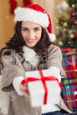 Composite image of festive brunette showing gift at christmas