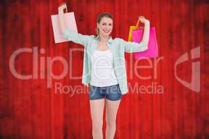 Composite image of smiling young woman holding up shopping bags