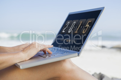 Composite image of woman sitting on beach using her laptop