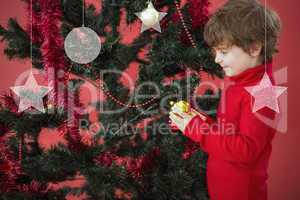 Composite image of festive little boy hanging a bauble