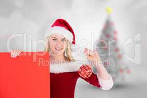 Composite image of festive cute blonde holding poster and bauble