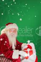 Composite image of father christmas taking red gift in his bag