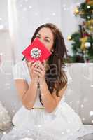 Composite image of brunette showing gift on the couch at christmas
