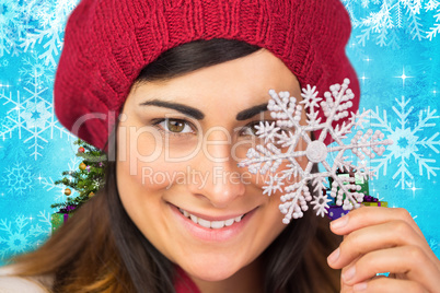 Composite image of smiling brunette in hat holding snowflake
