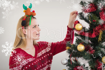 Composite image of woman hanging christmas decorations on tree