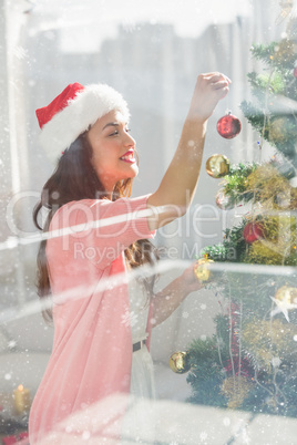 Composite image of festive brunette decorating a christmas tree