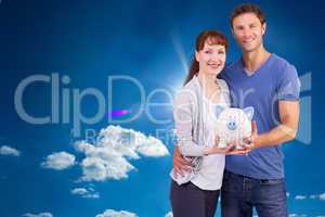 Composite image of couple holding a white piggy bank