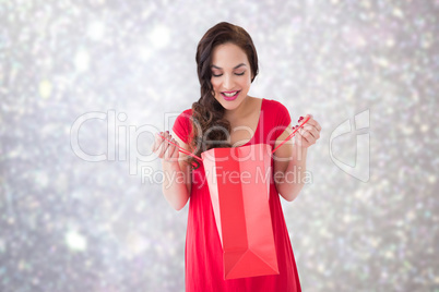 Composite image of stylish brunette in red dress opening gift ba