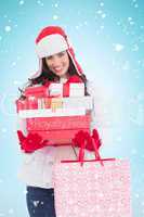 Composite image of brunette in winter clothes holding many gifts