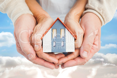 Composite image of couple holding small model house in hands