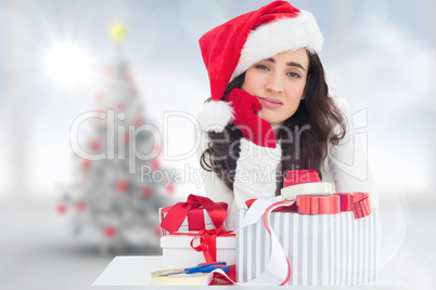 Composite image of unsure brunette in santa hat packing gifts