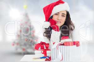 Composite image of unsure brunette in santa hat packing gifts