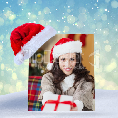 Composite image of festive brunette showing gift at christmas