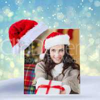 Composite image of festive brunette showing gift at christmas