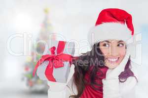 Composite image of surprised brunette in santa hat holding gift