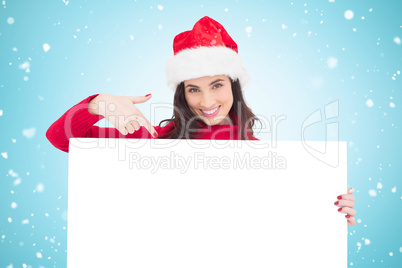 Composite image of pretty brunette in santa hat pointing white p