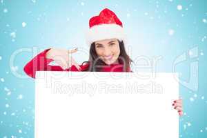 Composite image of pretty brunette in santa hat pointing white p