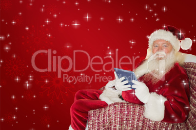 Composite image of smiling santa using tablet on the armchair