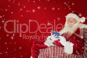 Composite image of smiling santa using tablet on the armchair