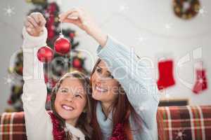 Composite image of festive mother and daughter holding baubles