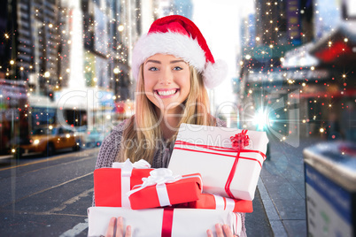 Composite image of festive blonde holding pile of gifts