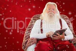 Composite image of smiling santa using tablet on the armchair