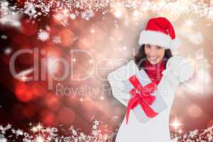 Composite image of excited brunette in santa hat giving gift