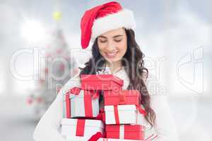 Composite image of festive brunette holding pile of gifts