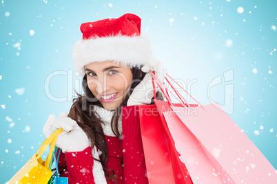 Composite image of festive brunette in winter wear holding shopp