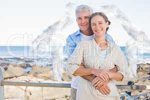Composite image of happy casual couple hugging by the coast