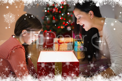 Composite image of festive mother and daughter opening a glowing