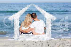 Composite image of affectionate couple sitting on the sand at th
