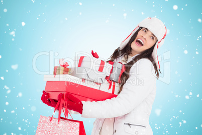 Composite image of brunette in winter clothes holding many gifts