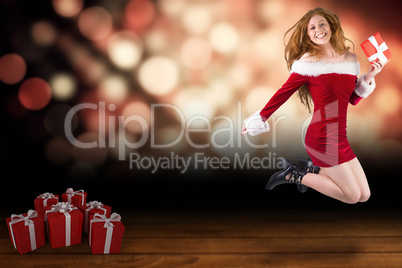 Composite image of festive redhead jumping with gift