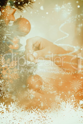 Composite image of woman hanging christmas decorations on tree