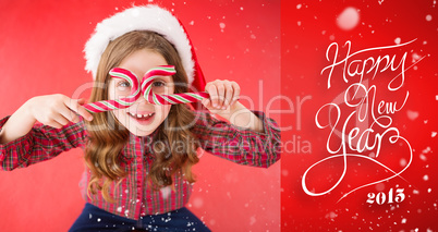 Composite image of happy little girl in santa hat holding candy