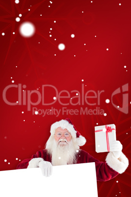 Composite image of santa shows a present while holding sign