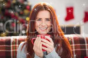 Composite image of festive redhead holding mug on couch