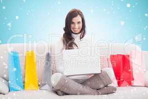 Composite image of pretty brunette using laptop on the couch