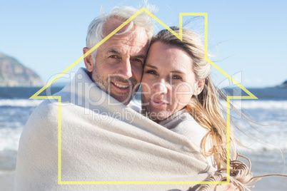 Composite image of smiling couple wrapped up in blanket on the b