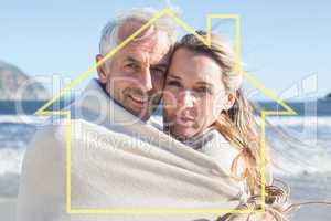 Composite image of smiling couple wrapped up in blanket on the b