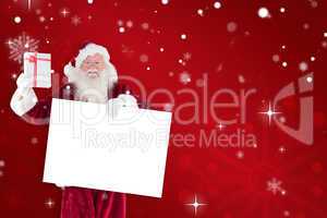 Composite image of santa shows a present while holding sign