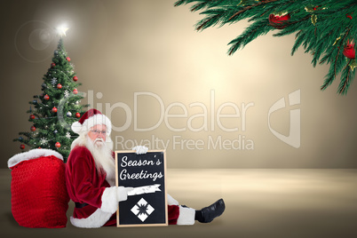 Composite image of santa sits leaned on his bag with a board