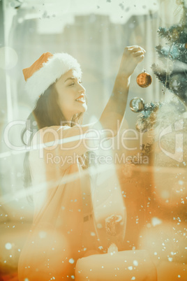Composite image of festive brunette decorating a christmas tree