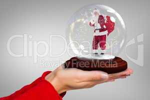 Composite image of hand holding santa snow globe