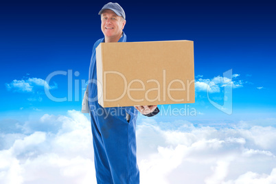 Composite image of happy delivery man showing cardboard box