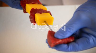 Hands of chef or professional chef making a professional cook red meat skewer and mango DETAIL